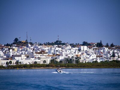 Distant view across body of water of Ayamonte town with single motorboat moving towards, Spain