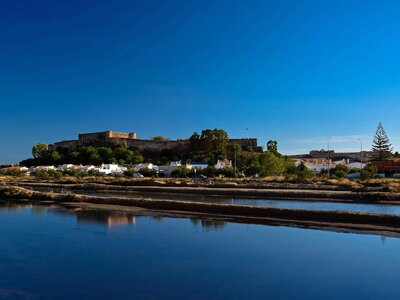 Town of Castro Marim and reflection of buildings in calm water in foreground with clear blue skies above, Portugal
