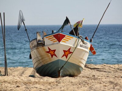 Front of decorated fishing boat with fishing equipment hanging out of boat on sand at beach, Monte Gordo, Portugal
