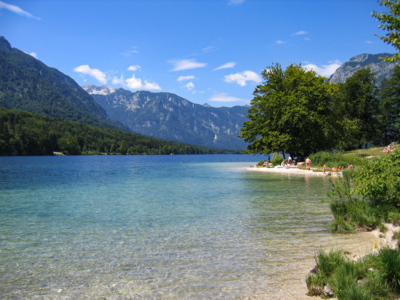 People in distance enjoying Bohinj lake on sunny day with mountains in distance, Slovenia